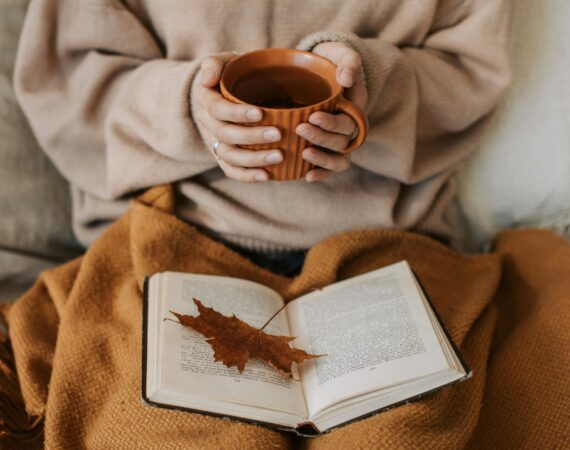 Woman reading a book with a coffee in hand under a brown blanket