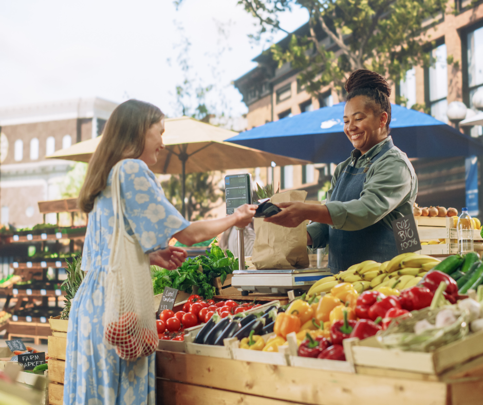 A woman buying vegetables from another woman at an outdoor farmers market booth